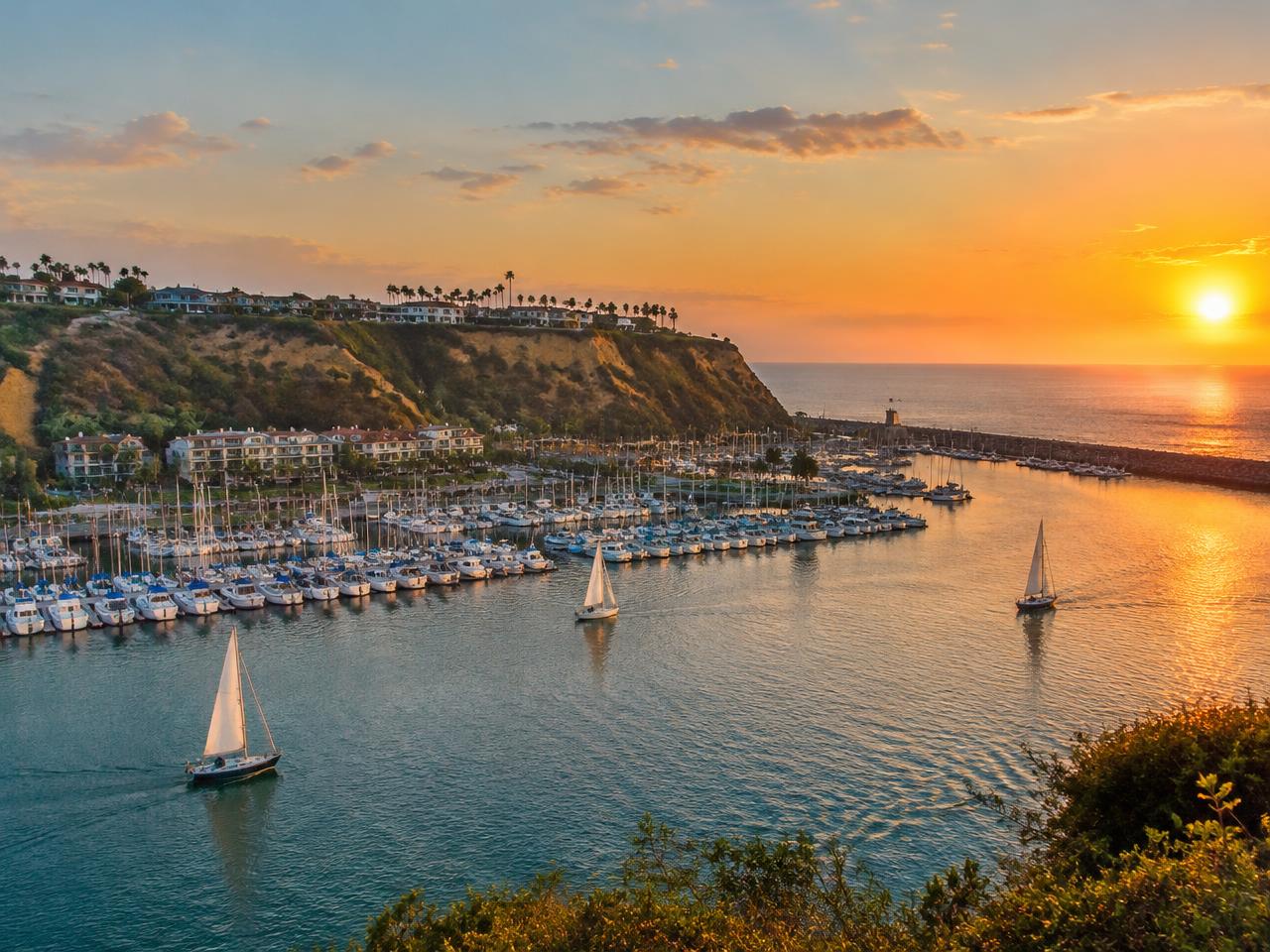 Dana Point harbor with sailboats below coastal bluffs at sunset